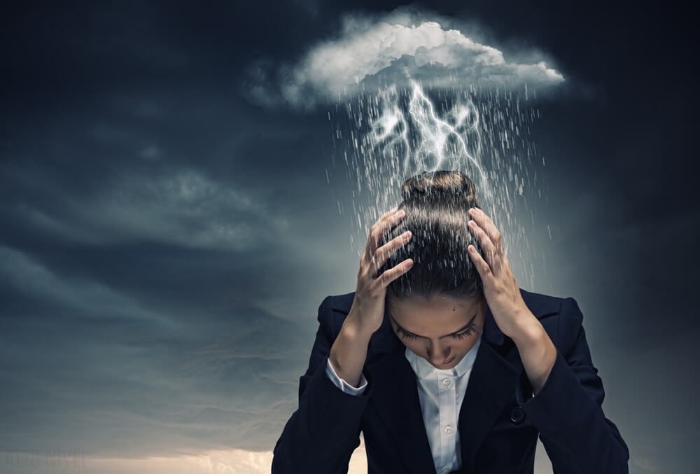 Vrouw die met haar hoofd omlaag gebogen staat omdat het vlak boven haar hoofd een stormwolk hangt als symbool voor bipolaire stoornis