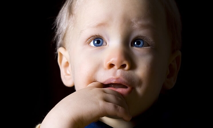 Jongetje met blauwe ogen dat met zijn vinger in zijn mond omhoog kijkt