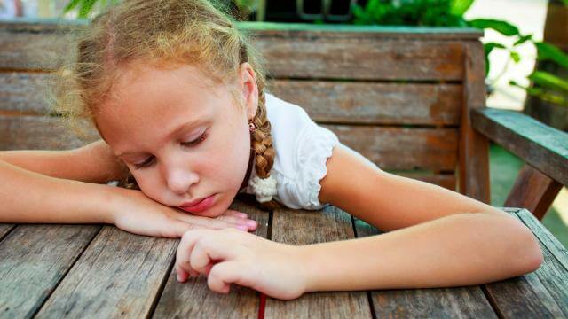 Meisje dat doelloos en ongelukkig over een tafel hangt als voorbeeld van depressie bij kinderen