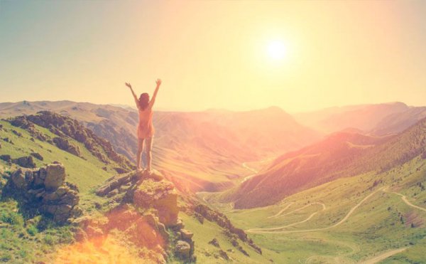 Vrouw die van blijdschap haar armen in de lucht steekt want ze heeft de top van de berg bereikt en kan taai zijn