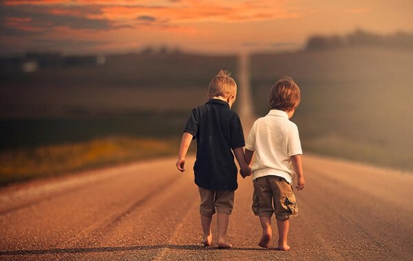 Twee jongetjes die samen op blote voeten over een grote weg lopen