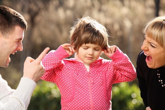 Klein meisje houdt haar oren dicht voor het geschreeuw van haar ouders, die niet weten dat schreeuwen tegen je kind niets oplost