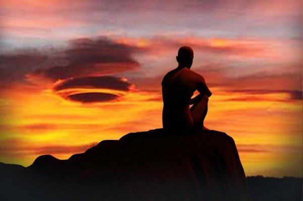 Man die van een rots zit te kijken naar de zonsopgang