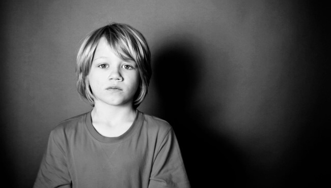 Jongetje dat voor een zwarte achtergrond staat en droevig voor zich uit kijkt als voorbeeld van die vergeten kinderen