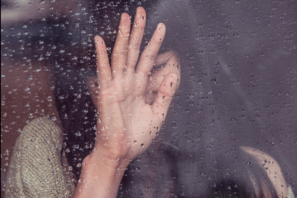 Vrouw die huilend tegen een nat raam aanleunt
