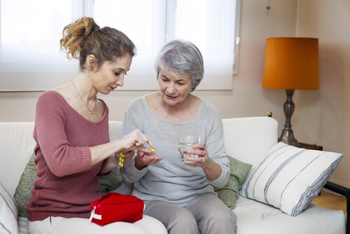 Vrouw die oudere vrouw helpt met het innemen van haar medicijnen als voorbeeld van mantelzorg