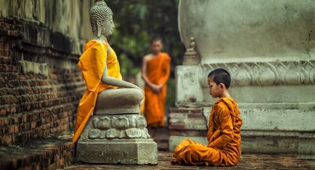 Boeddhistische monnik die mediteert bij een beeld van Boeddha