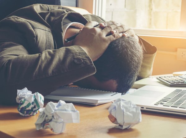 Man die uit frustratie zijn hoofd op tafel legt, want omgaan met negatieve mensen kan zeer frustrerend zijn