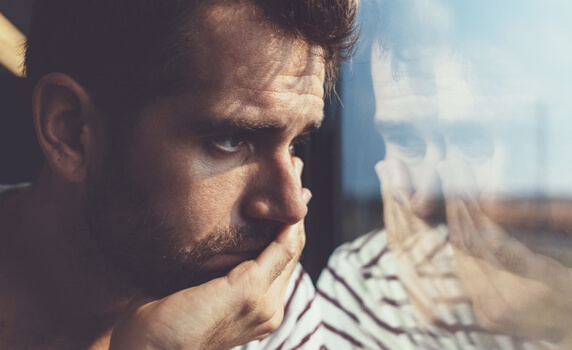 Man die bedroefd uit het raam kijkt