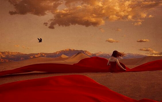 Vrouw met een rode jurk aan die in haar eentje in de woestijn zit om de emotionele wond op haar ziel te genezen