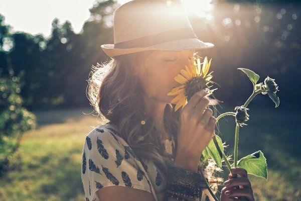 Vrouw die aan een zonnebloem ruikt, want positief denken draagt bij aan geluk