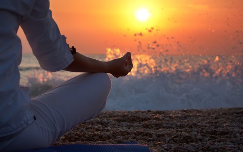 Mediteren op het strand bij zonsondergang dankzij de kennis uit boeken over meditatie