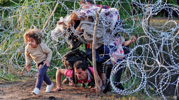 Vluchtelingen die onder een hek van prikkeldraad door kruipen