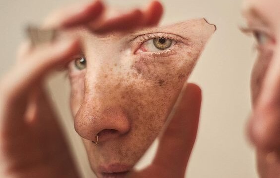 Vrouw kijkt naar zichzelf in gebroken spiegel