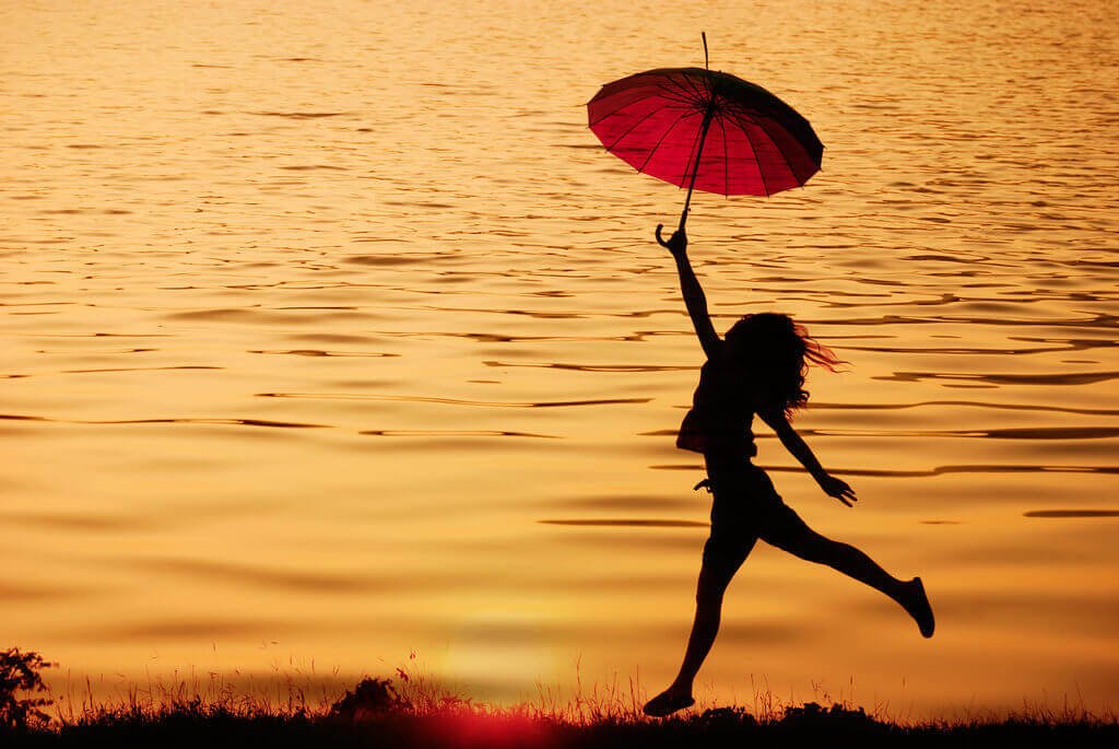 Vrouw die met een paraplu langs het water loopt en zich laat leiden door haar intrinsieke motivatie