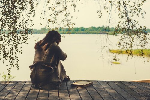 Vrouw die op een steiger aan een meer zit en haar gebroken hart vermijden wil