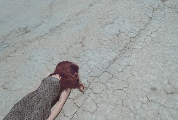 Meisje dat met haar haar over haar gezicht op droog landschap ligt, omdat ze last heeft van paniekaanvallen