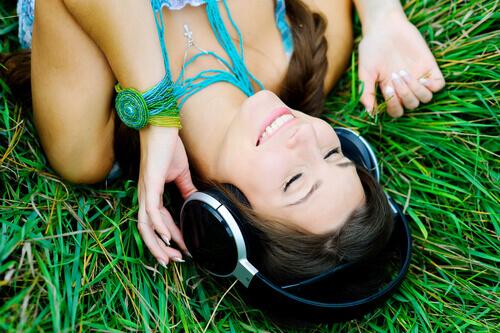 Vrouw die in het gras muziek ligt te luisteren