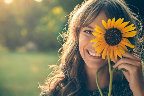 Meisje dat een zonnebloem voor haar oog houdt en glimlacht, want je lach kan de wereld veranderen