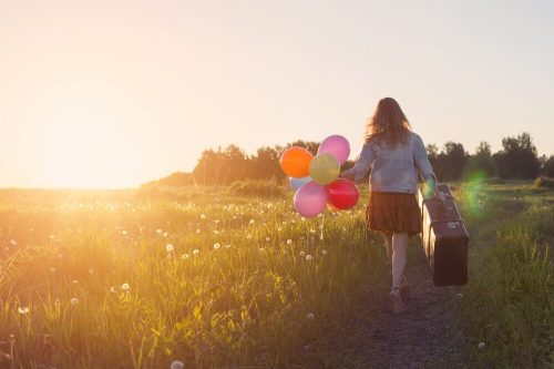 Vrouw met koffer en ballonnen in een veld