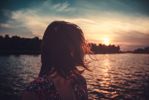 Vrouw die over het water naar de zon kijkt