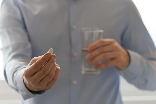 Man met pil in de hand, en een glas water