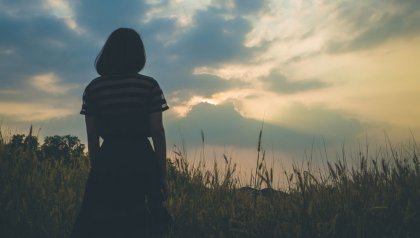 Vrouw met sterk zelfbewustzijn staat in een veld bij zonsondergang
