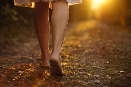 Een vrouw loopt op blote voeten over een zandweg