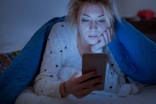 Een vrouw kijkt naar haar mobiele telefoon in bed