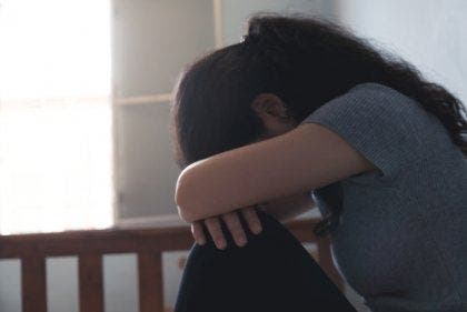 Een vrouw leunt met haar gezicht op haar knieën