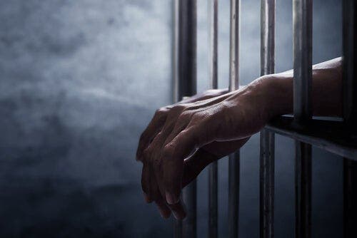 Twee handen steken door de tralies van een gevangenis