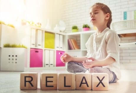 Het woord relax uitgespeld in houten blokken met een kind in meditatiehouding
