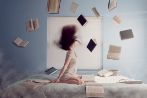 Een vrouw zit rechtop in bed met om haar heen vliegende boeken