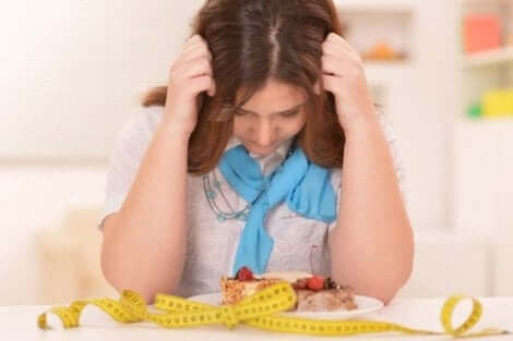Een vrouw zit met haar handen in het haar boven een bord eten en een meetlint