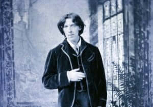 Oscar Wilde in een zwartwit foto met zijn hand op zijn buik
