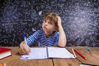 Een jongen zit aan een bureau met een schrijfblok en een pen