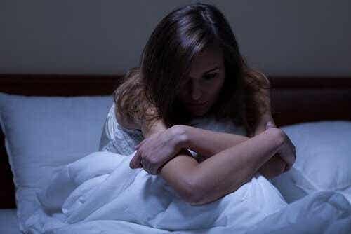 Een vrouw zit rechtop in bed met haar armen over haar knieën