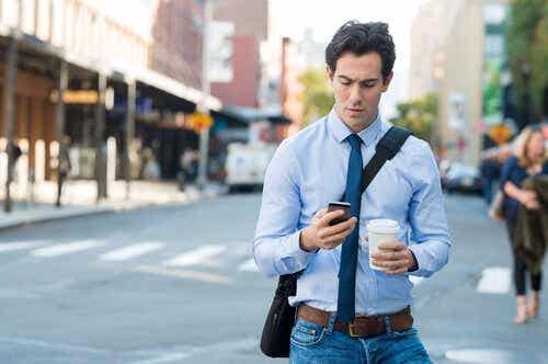 Een man loopt op straat en kijkt naar zijn mobiele telefoon