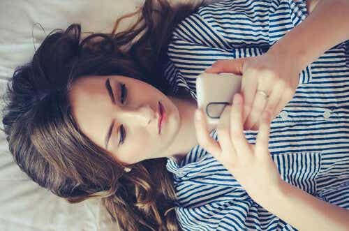 Een vrouw ligt op bed en kijkt naar haar mobiele telefoon